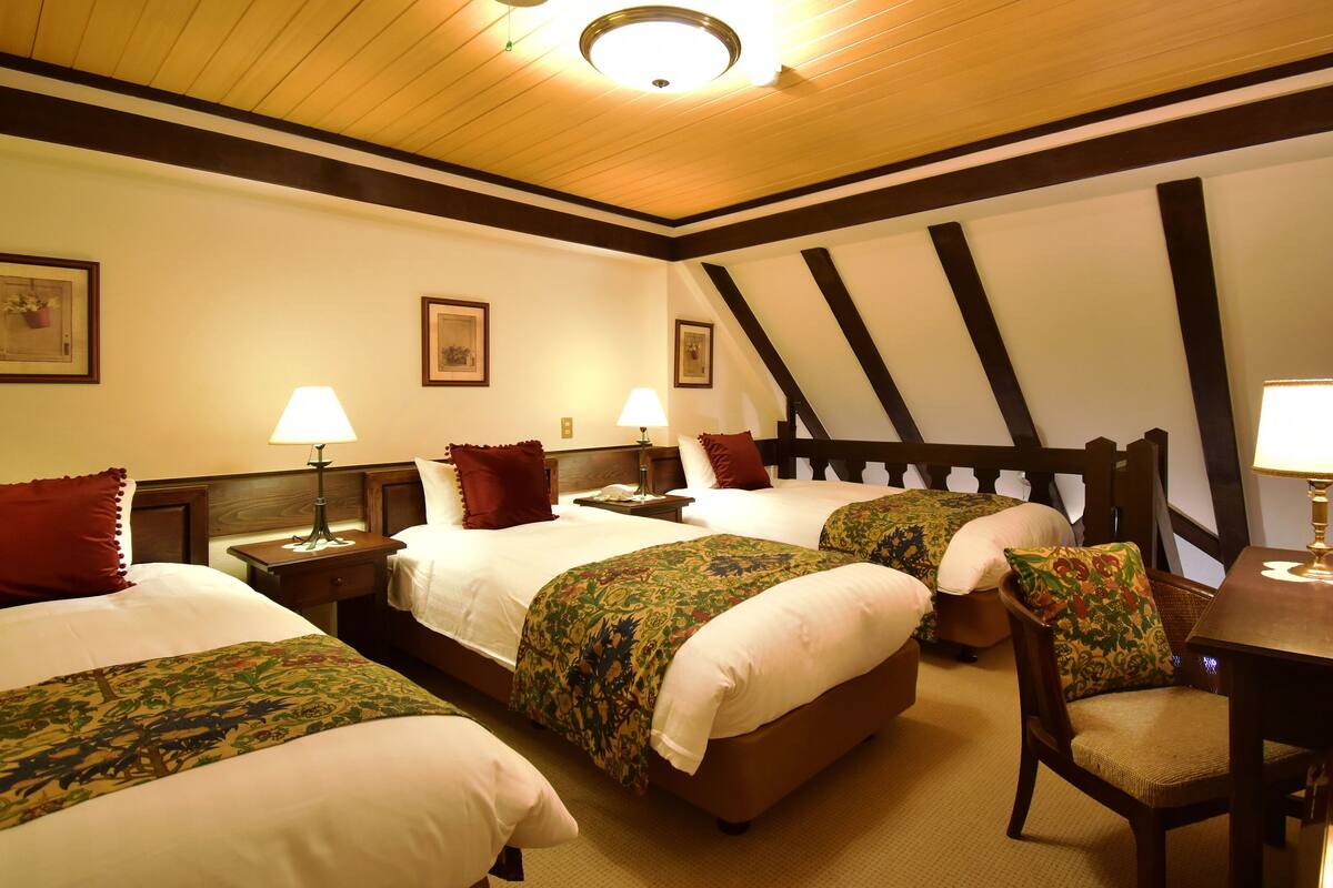 A hotel room with four beds, each with a different patterned bedspread, a wooden headboard, and a nightstand with a lamp.