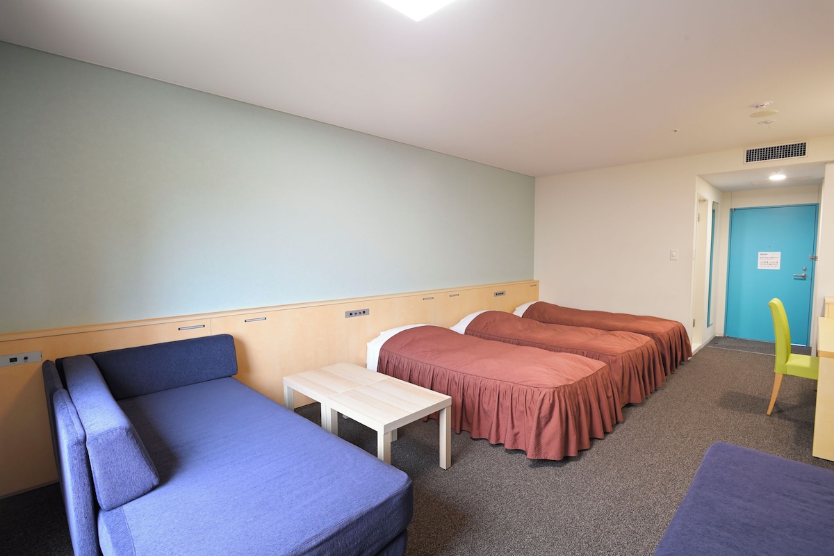 A room with a bed, a small table, a chair, and a blue sofa.
