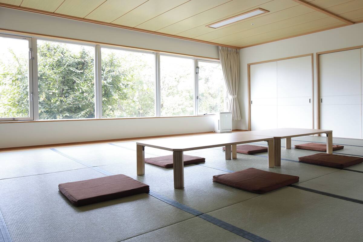 Una habitación con tatamis, una mesa baja, cojines, ventanas amplias y puertas correderas.