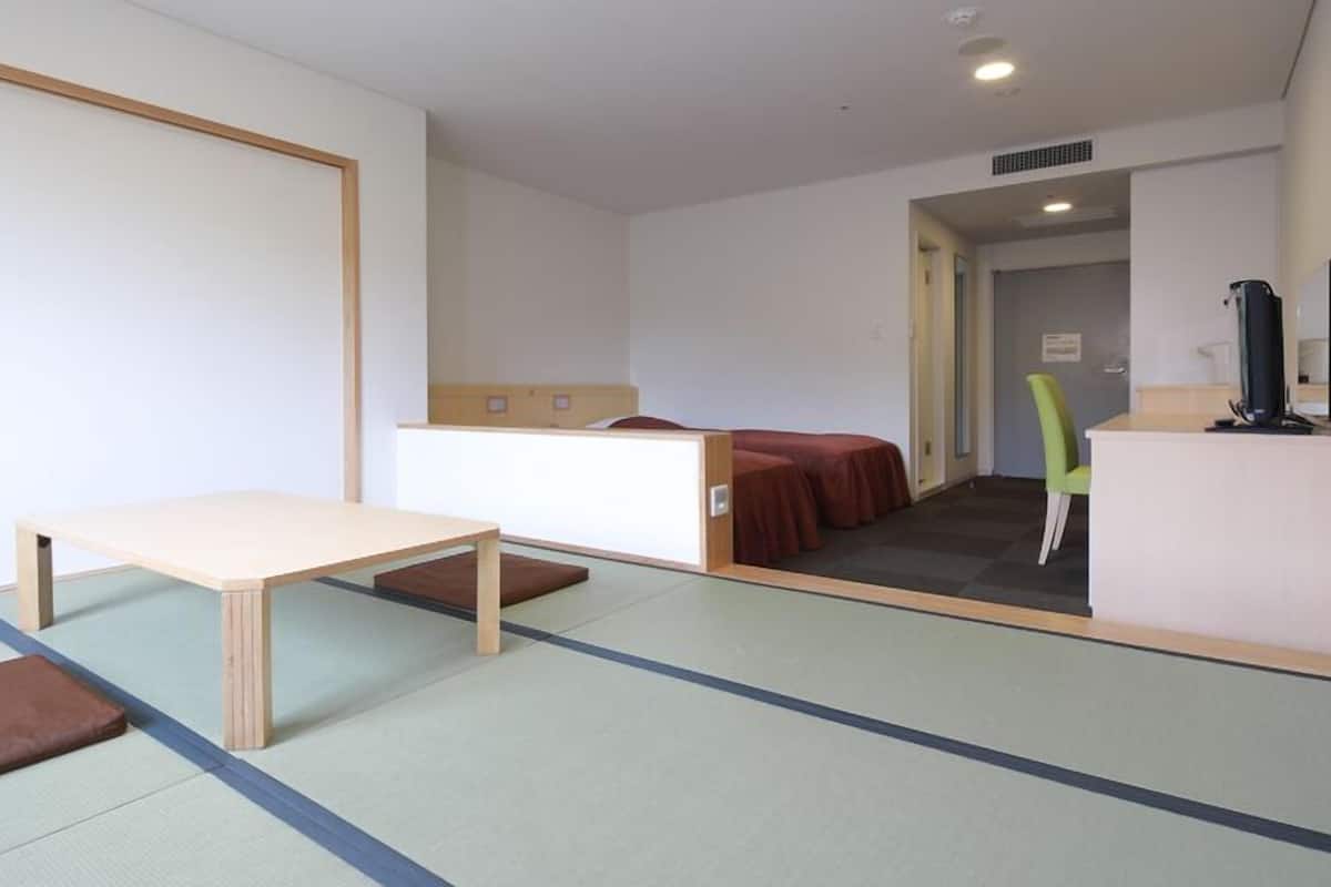 A room with a wooden table, a bench, a bed with a red bedspread, and a green chair.