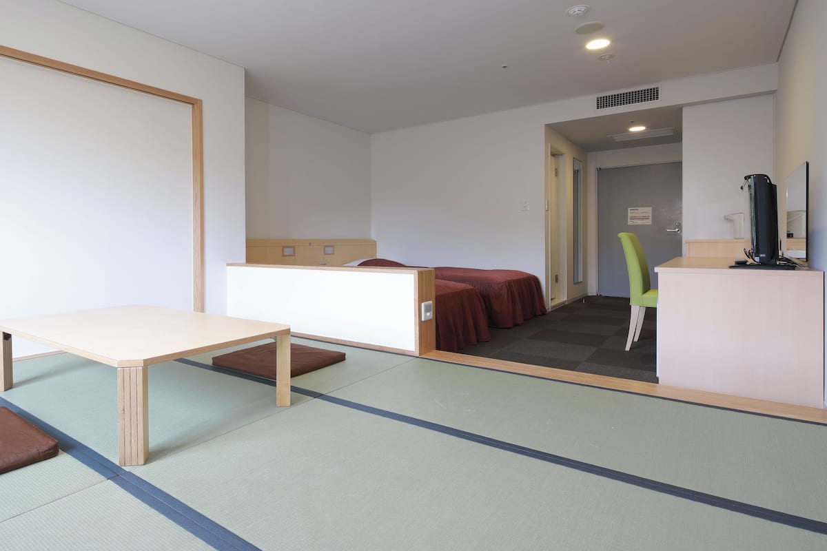 Una habitación con esteras de tatami, una mesa de madera, una cama y un mostrador de recepción.