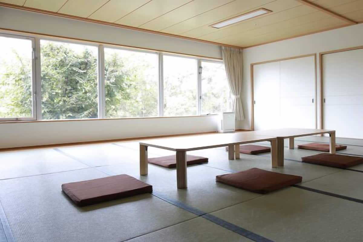 Una habitación con suelo de tatami, una mesa baja y cojines, ventanas amplias y puertas correderas.