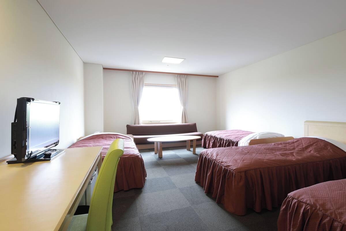 Habitación de hotel con escritorio, dos camas, sofá, una mesita y televisor.