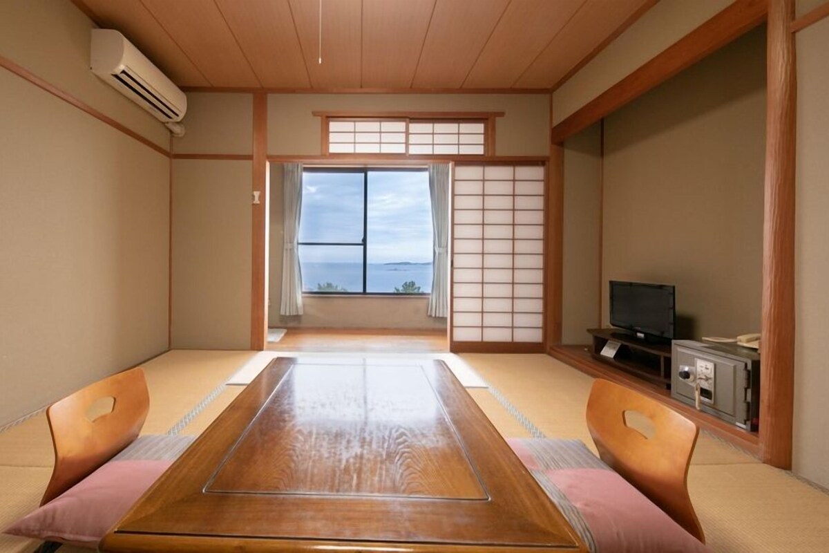 A traditional Japanese room with tatami flooring, a low wooden table, and a television on a wooden cabinet.