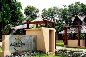 The entrance of Aurora Resort with a stone sign, wooden structures, and lush greenery.