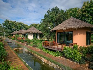 A row of thatched-roof cottages with a water channel running alongside them. - Aurora Resort Chiang Dao (Chiang Dao)