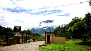 A rural setting with a gravel path leading to a traditional structure with a thatched roof, surrounded by greenery and a mountain backdrop. - Aurora Resort Chiang Dao (Chiang Dao)