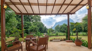 A covered outdoor seating area with wooden furniture and a view of a lush garden and mountains. - Aurora Resort Chiang Dao (Chiang Dao)