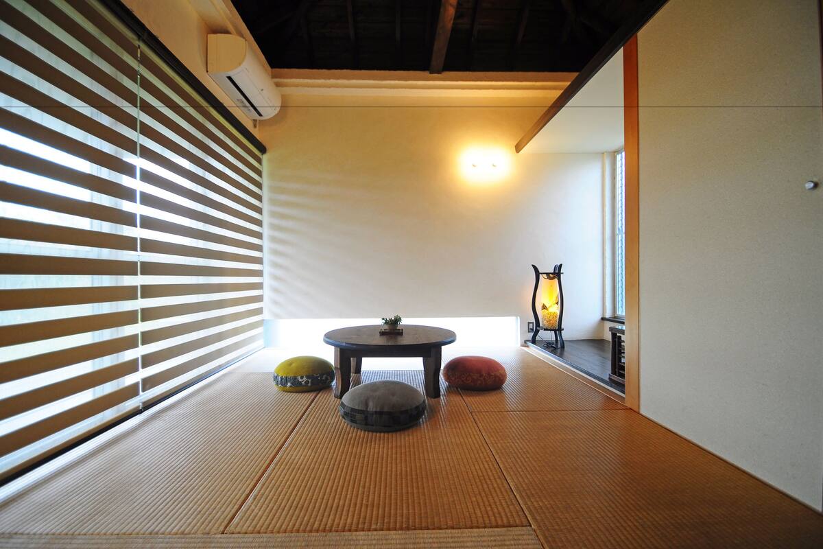 Um espaço com tatames, tela deslizante shoji, uma mesa redonda pequena e almofadas.