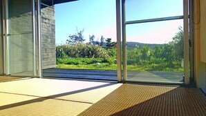 A room with large glass doors leading to an outdoor area with a view of greenery and hills. - Fu-rai-so Private Villa (Nakijin)
