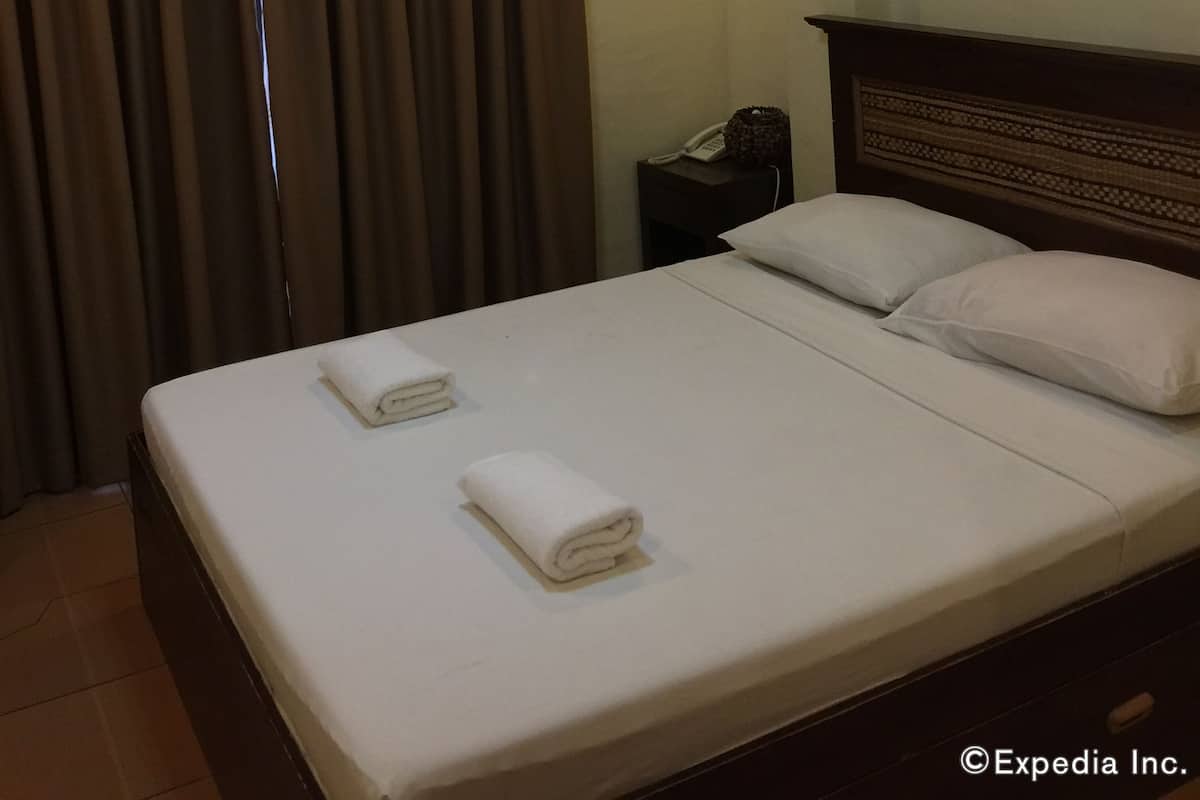 A hotel room with a bed, a bedside table with a phone, an air conditioning unit, and a ceiling light.