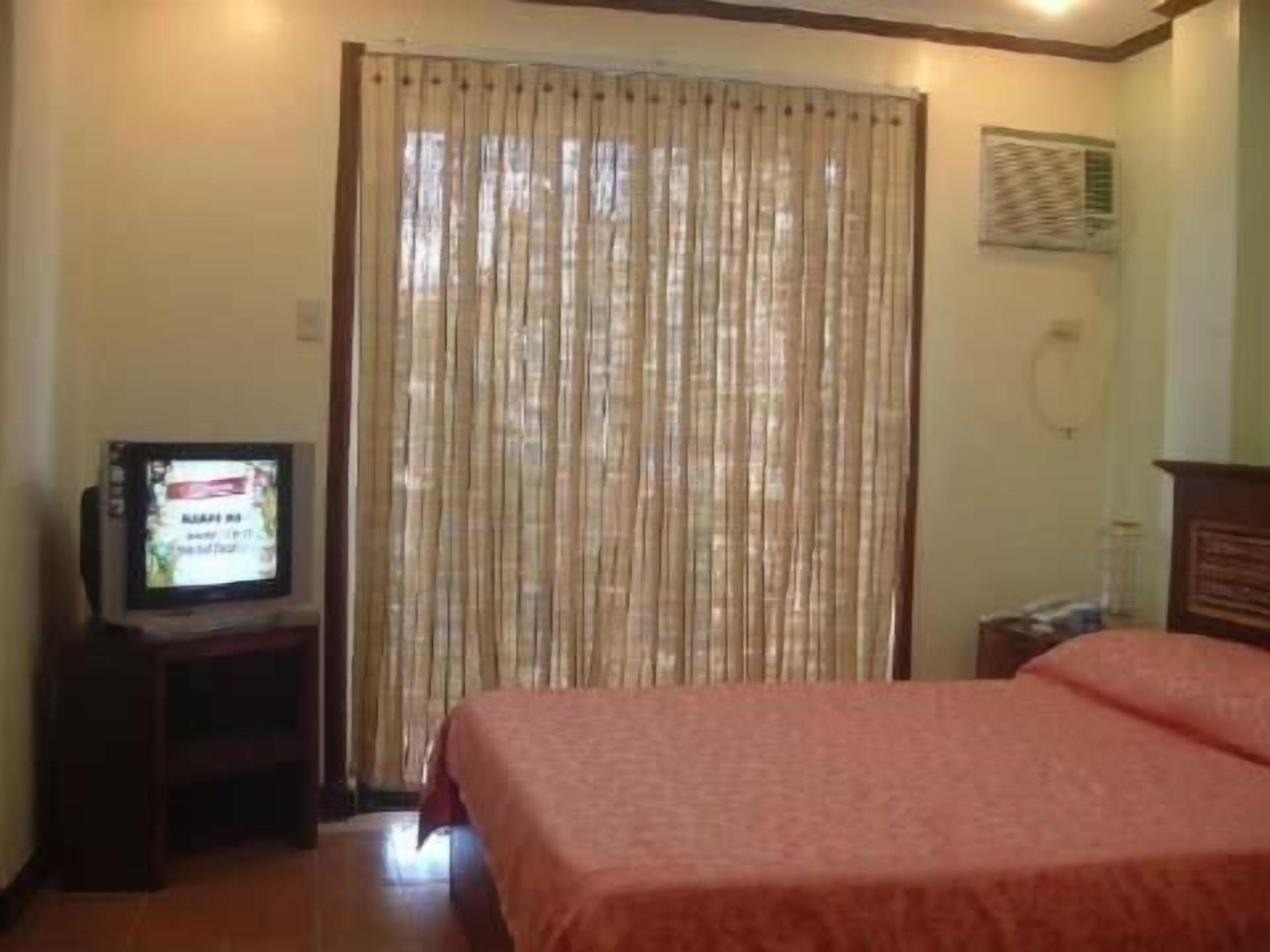 A hotel room with a bed, a television on a stand, and a curtain.