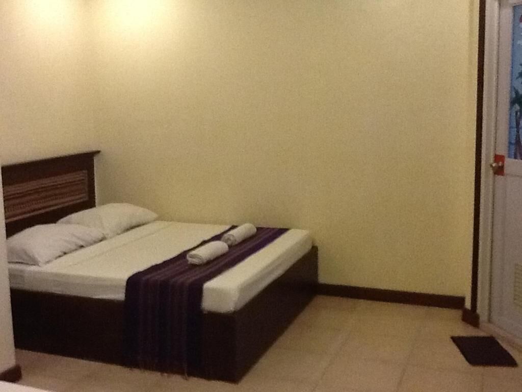 A single bed with a wooden headboard, a white mattress, and a purple blanket.