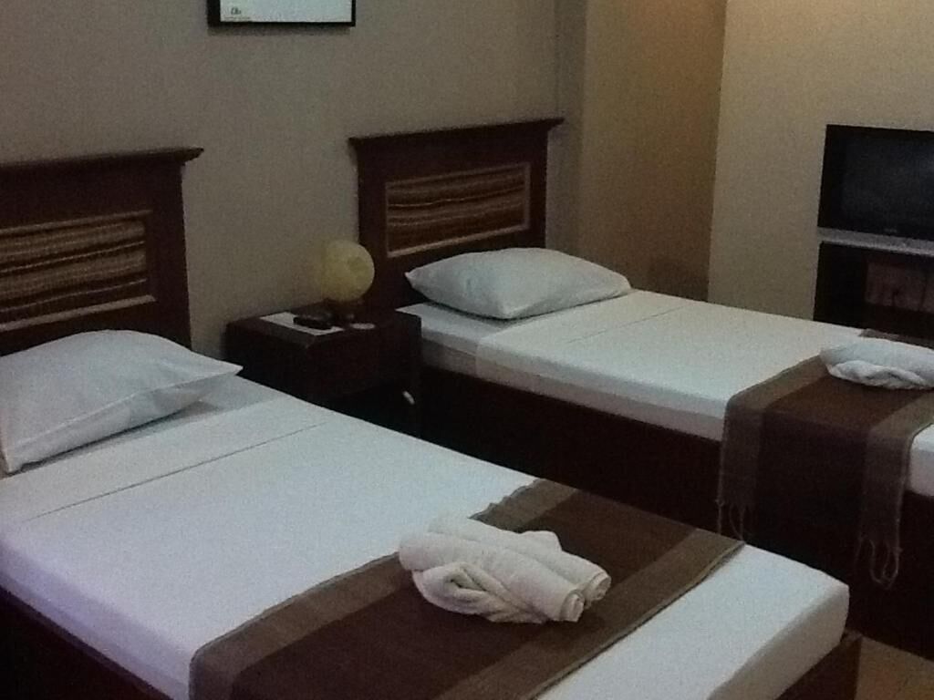 Two single beds with wooden headboards, a nightstand with a lamp, and a television on the wall.