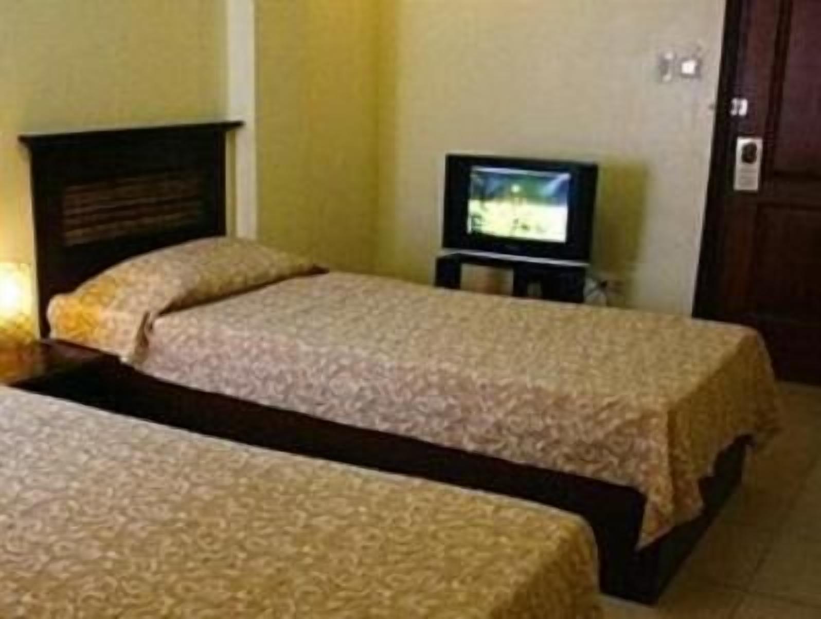Una habitación con dos camas, un televisor sobre un mueble bajo y un cabecero de madera.