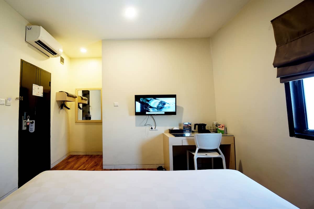 A hotel room with a bed, a desk with a chair, a TV, and an air conditioning unit.
