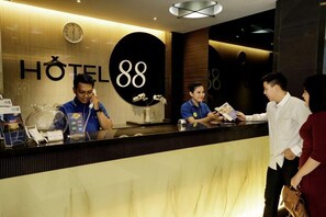 Una recepción de hotel con un reloj, el número grande '88', y un mostrador con una separación de vidrio.