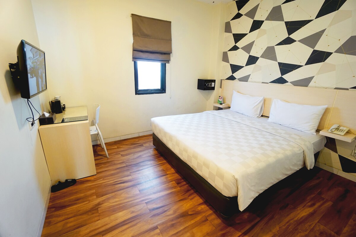 A hotel room with a bed, a desk, a chair, a TV, a window, and a geometric wall design.