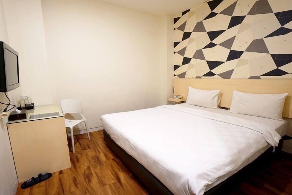 A hotel room with a bed, a desk, a chair, and a wall with a geometric pattern.