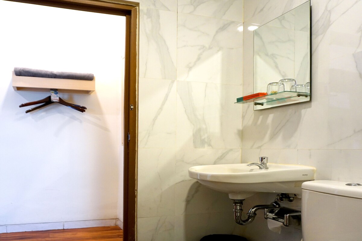 A bathroom with a toilet, sink, and mirror. There is a towel on the toilet, and a towel rack on the wall.