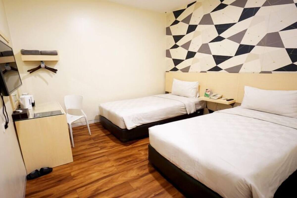 A hotel room with two beds, a desk, a chair, a TV, and a geometric-patterned wall.