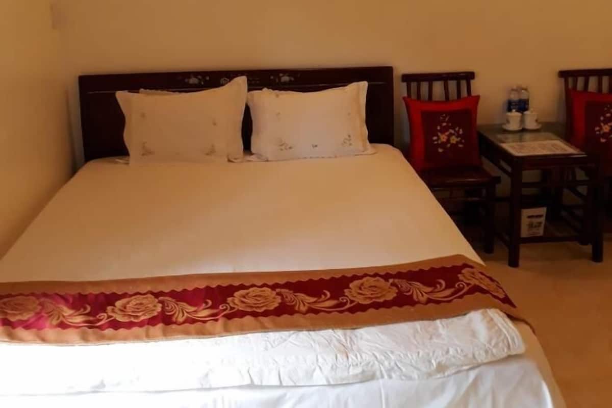 Una cama bien hecha con una colcha blanca y roja, un cabecero de madera y dos sillas rojas con una mesita de noche al lado.