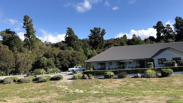 Une maison avec un toit en métal, entourée d’une pelouse bien entretenue et d’une colline boisée en arrière-plan.