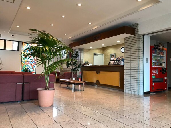 A hotel reception area with a reception desk, seating area, and a Coca-Cola vending machine.