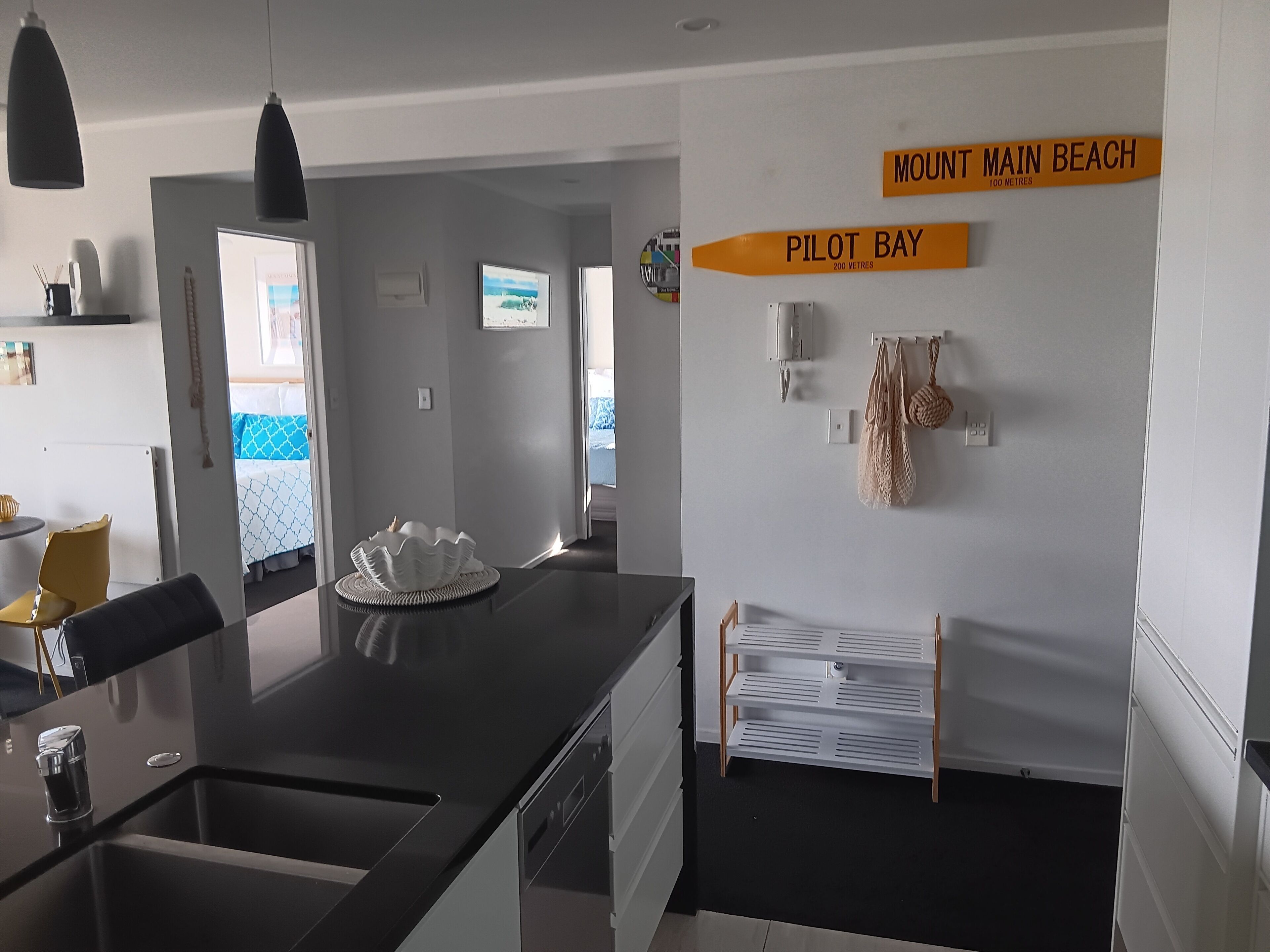 A modern kitchen with a central island, a dining area with a yellow chair, and a view of the beach.