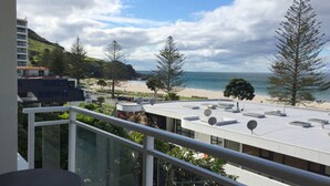 A balcony with a glass railing overlooking a beach and ocean. - The Atrium Apartments (Tauranga)