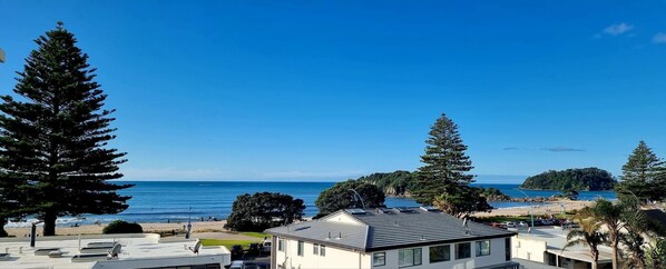 A coastal view with a beach, ocean, and a row of white buildings with a sloped roof.