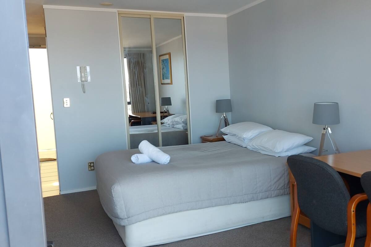 A hotel room with a bed, a desk, two lamps, a chair, and a mirror.