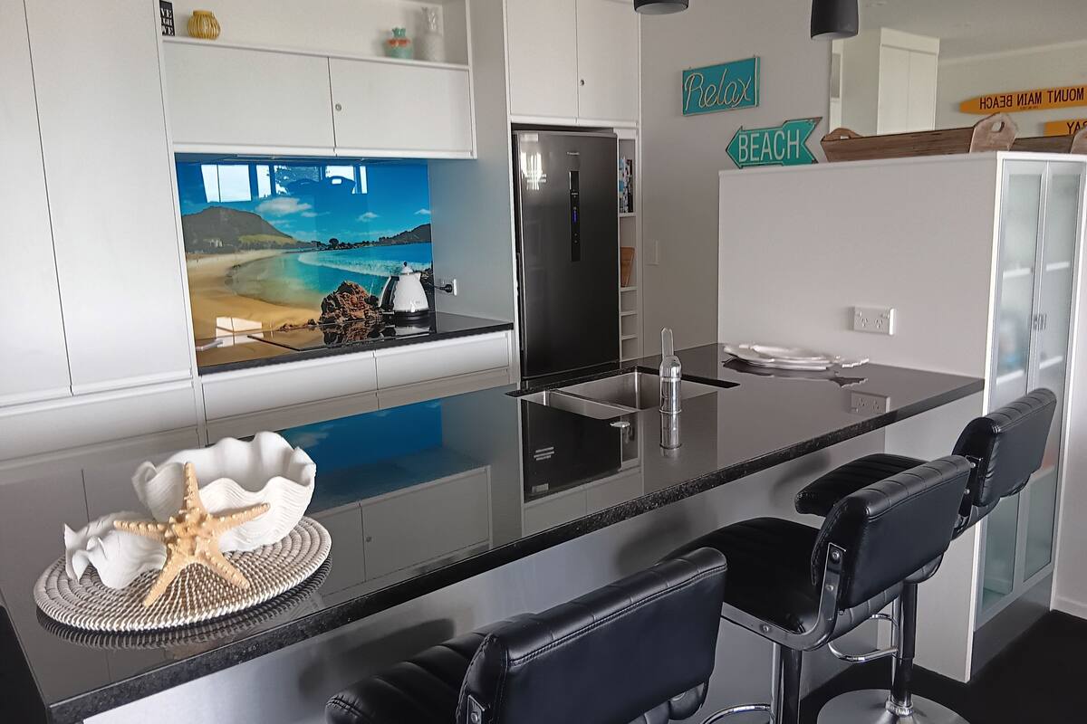 A modern kitchen with a central island, black bar stools, and a decorative starfish.