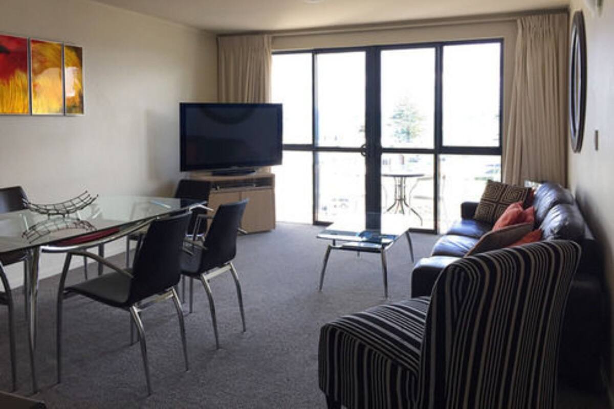 A modern living room with a glass dining table, black chairs, a striped sofa, and a flat-screen TV.
