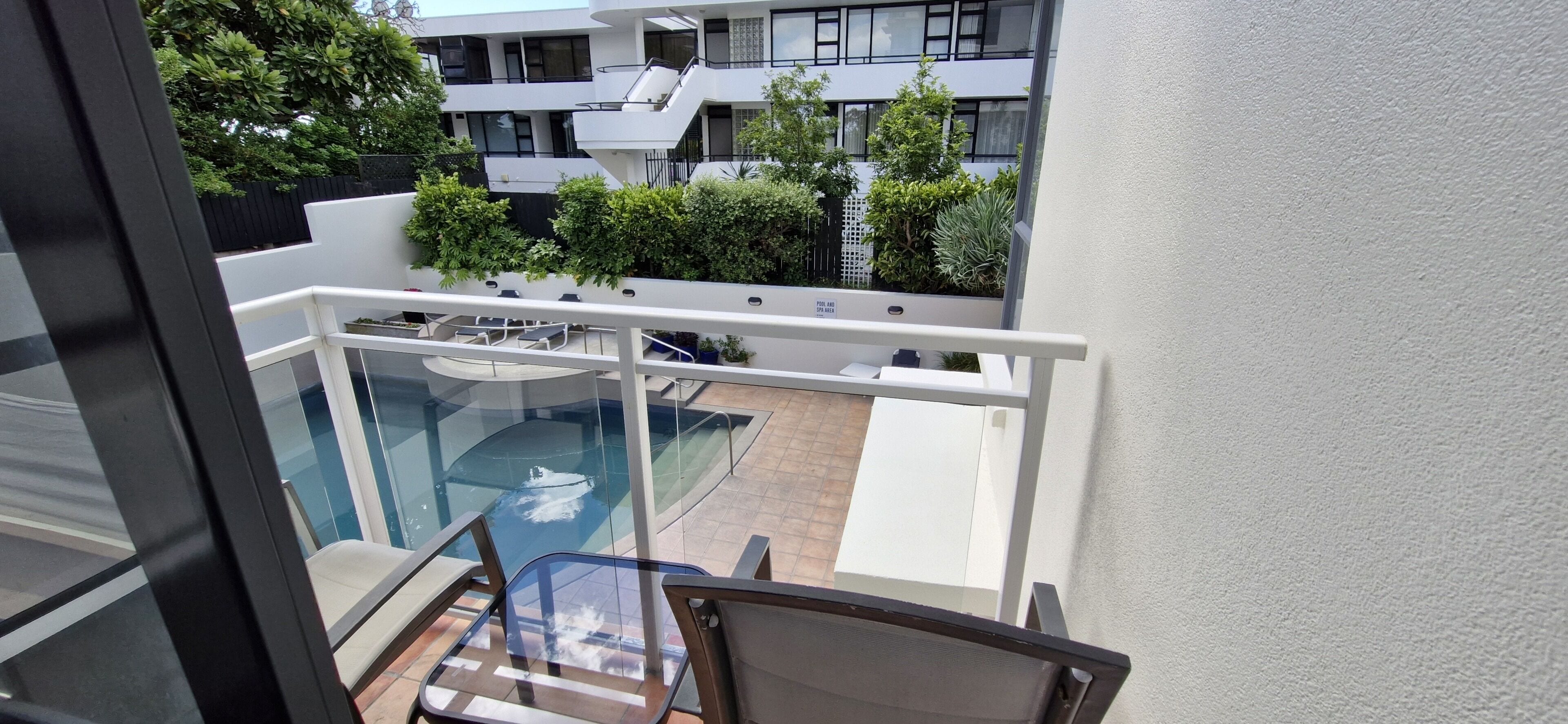 Ein Balkon mit Glastrennwand mit Blick auf einen Pool und einen Garten.