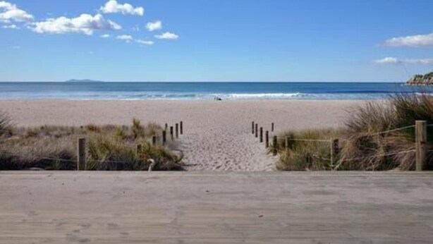 A beach with a wooden boardwalk leading to the water, surrounded by sand and sparse vegetation. - The Atrium Apartments (Tauranga)