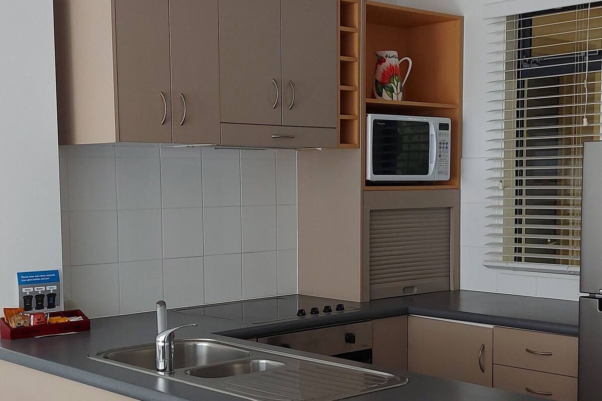 A modern kitchen with a central island, built-in cabinets, a microwave, and a window with blinds.