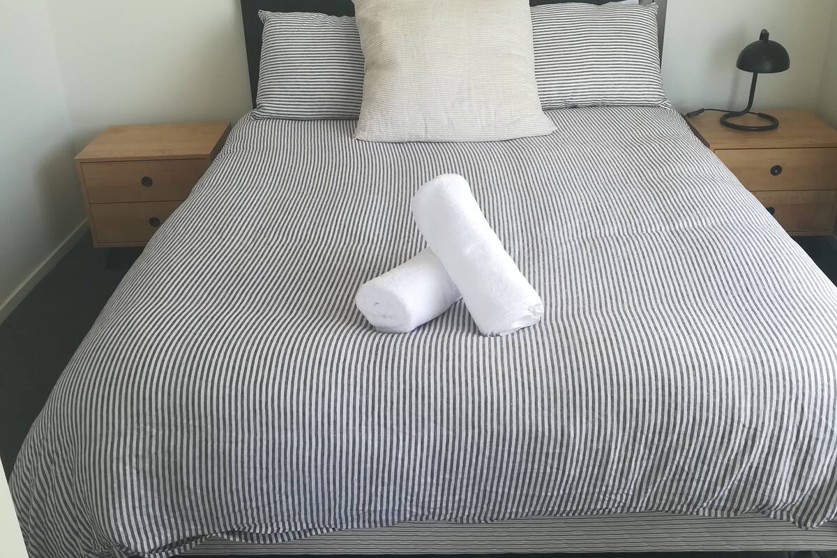 A neatly made bed with striped bedding, two pillows, and a rolled towel.