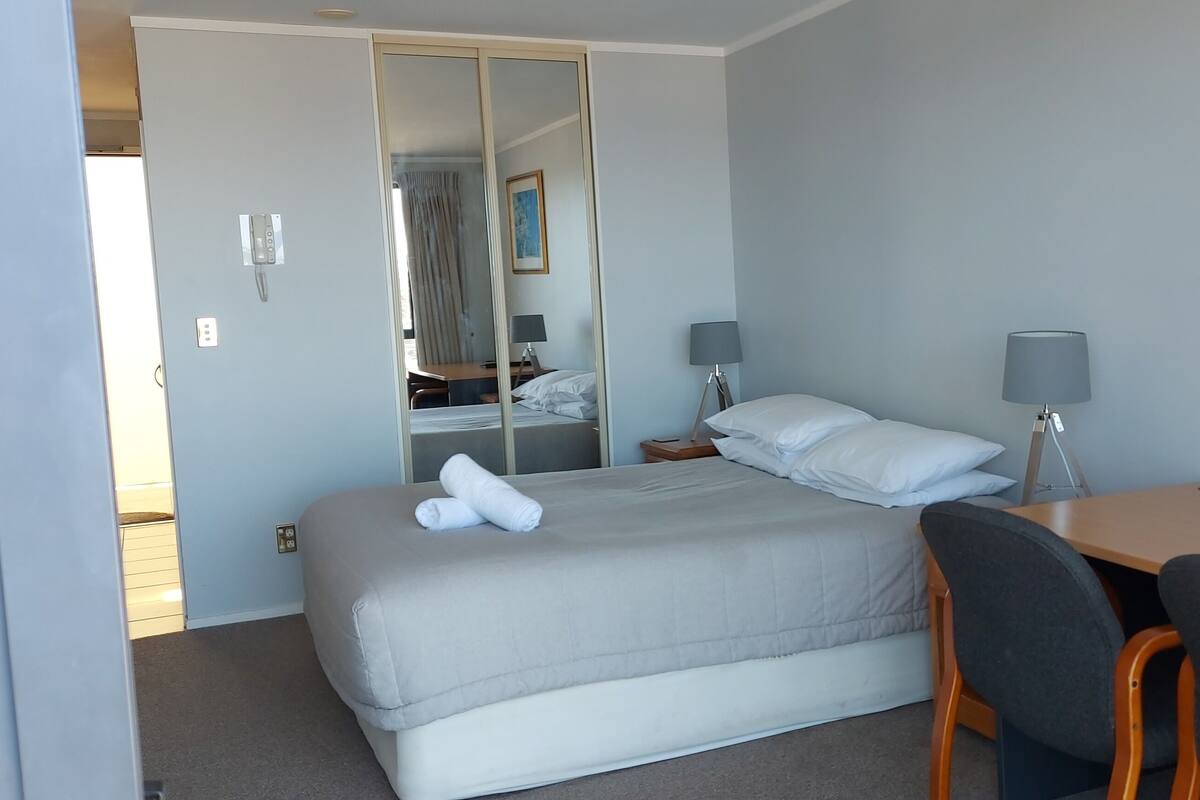 A hotel room with a bed, bedside tables, a desk, and a chair.
