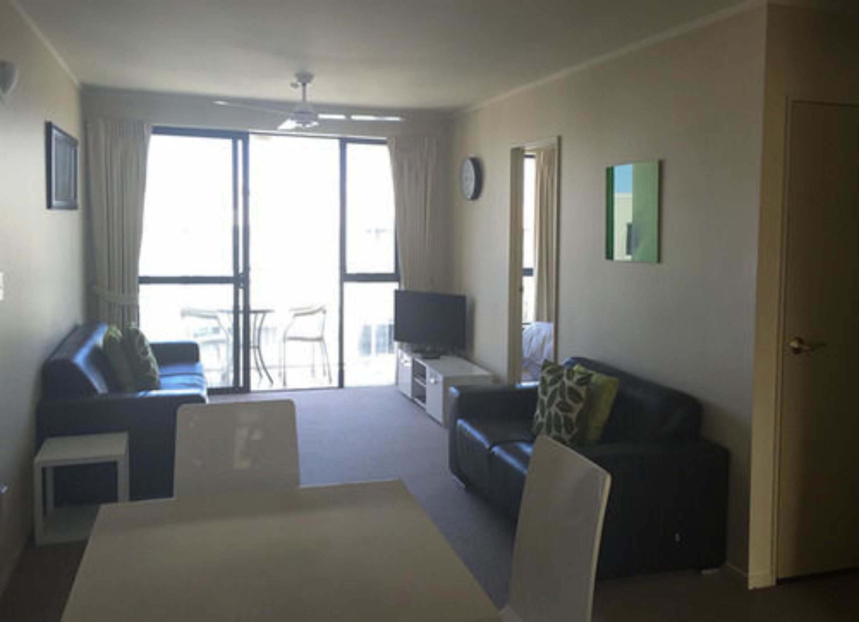 A living room with a sofa, a TV, a table, and a chair. There is a sliding glass door leading to a balcony.