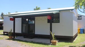 A small, single-story building with a flat roof and a covered entrance area. There are two potted plants outside, and a sign indicating a public phone.