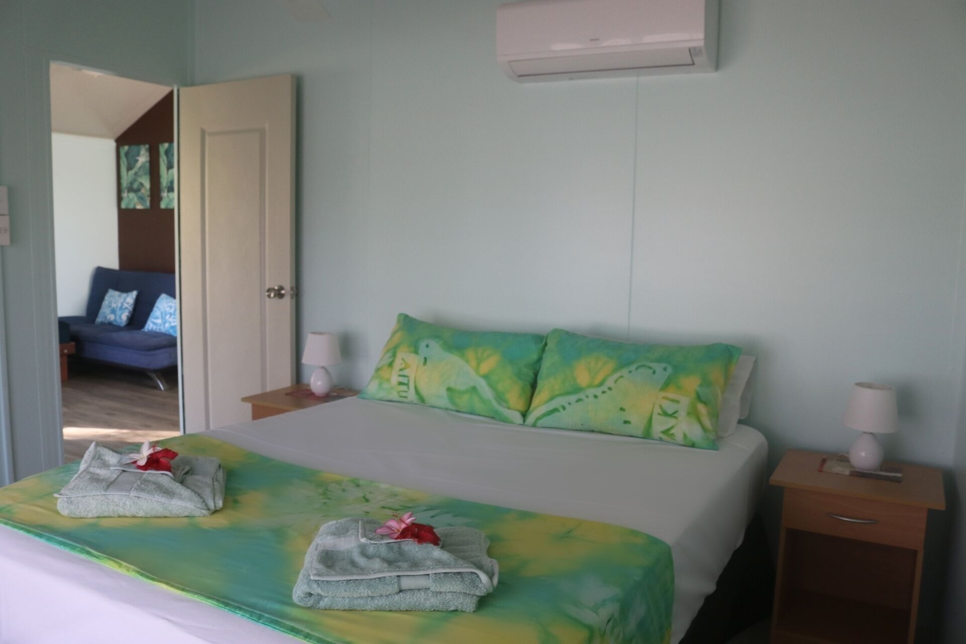 A bedroom with a bed, two pillows, a bedside table, a nightstand, and an air conditioning unit.