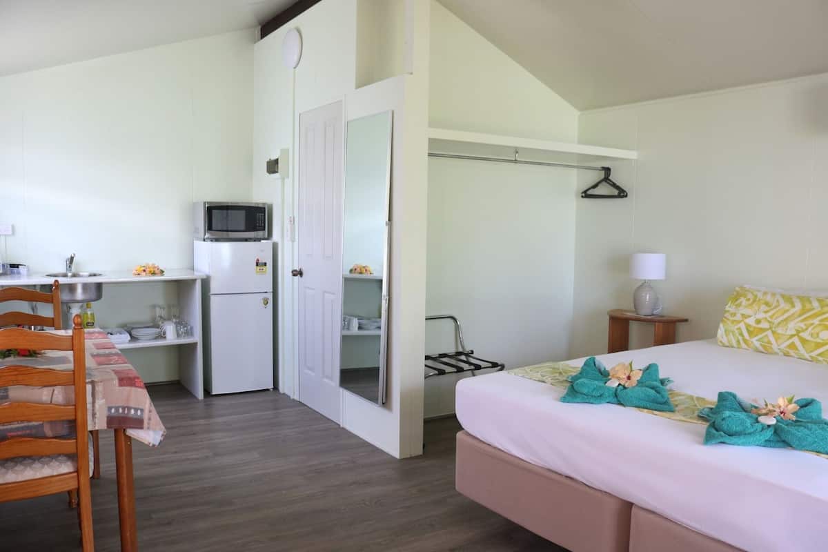 Ein kompaktes Hotelzimmer mit Bett, einer kleinen Küchenzeile, einem Schreibtisch mit Stuhl und einem Badezimmer mit Dusche.
