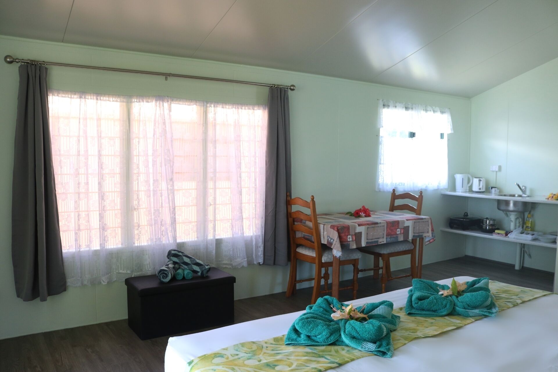 Une chambre d’hôtel avec un lit, une table, des chaises, une petite kitchenette et une fenêtre avec des rideaux.