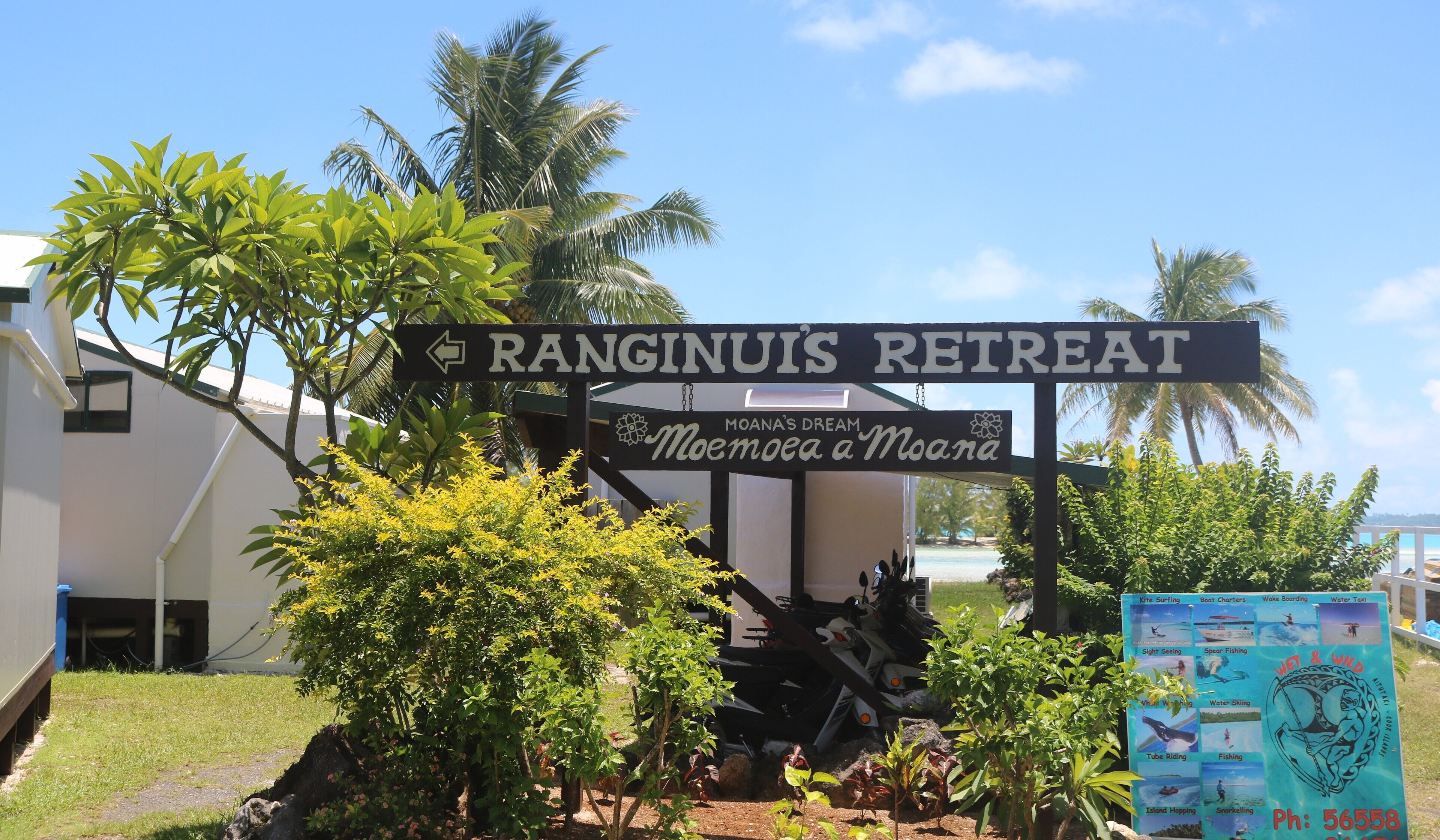 A sign for Ranginuiis Retreat with a directional arrow, surrounded by greenery and a view of the ocean.
