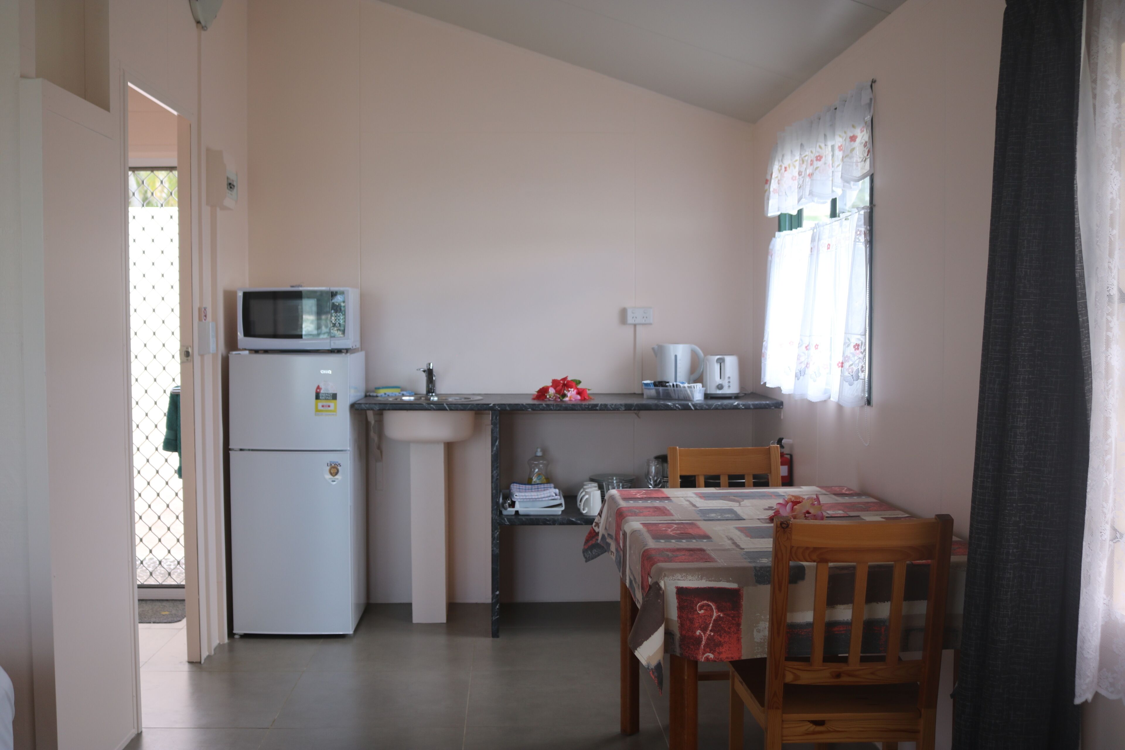 A compact kitchen with a refrigerator, microwave, sink, and a dining area with a table and chairs.
