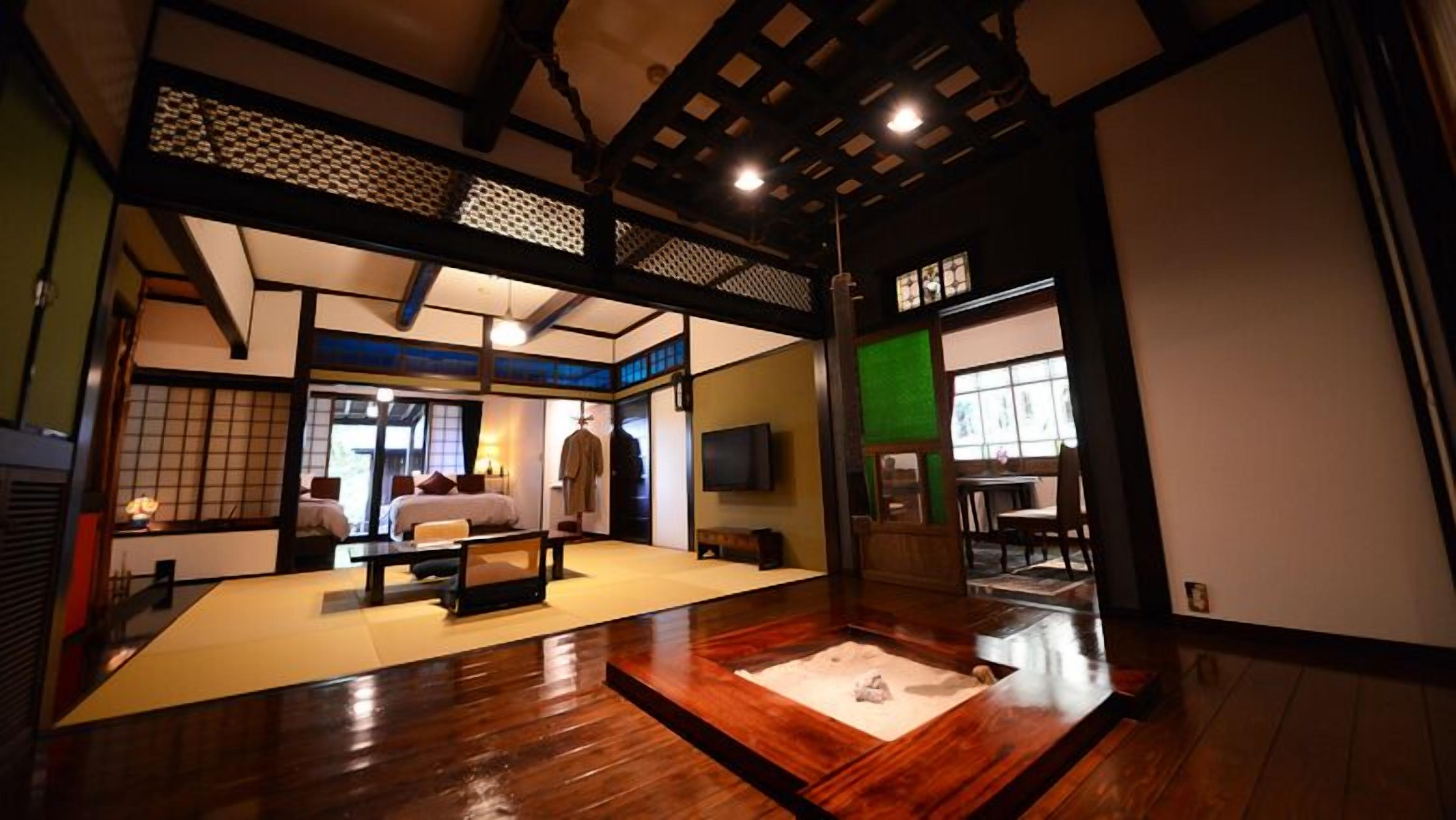 A traditional Japanese-style room with tatami flooring, a low table, a bed with pillows, and a television.