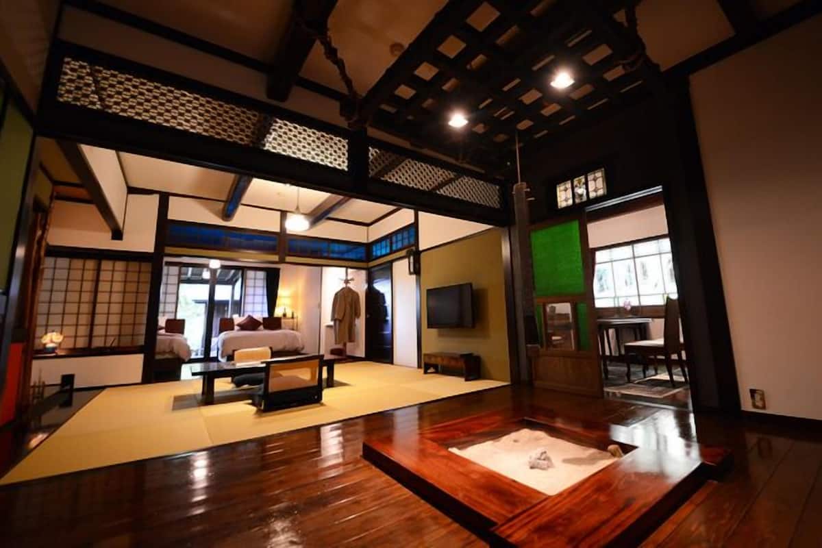A traditional Japanese-style room with tatami flooring, a low table, a bed with pillows, and a television.