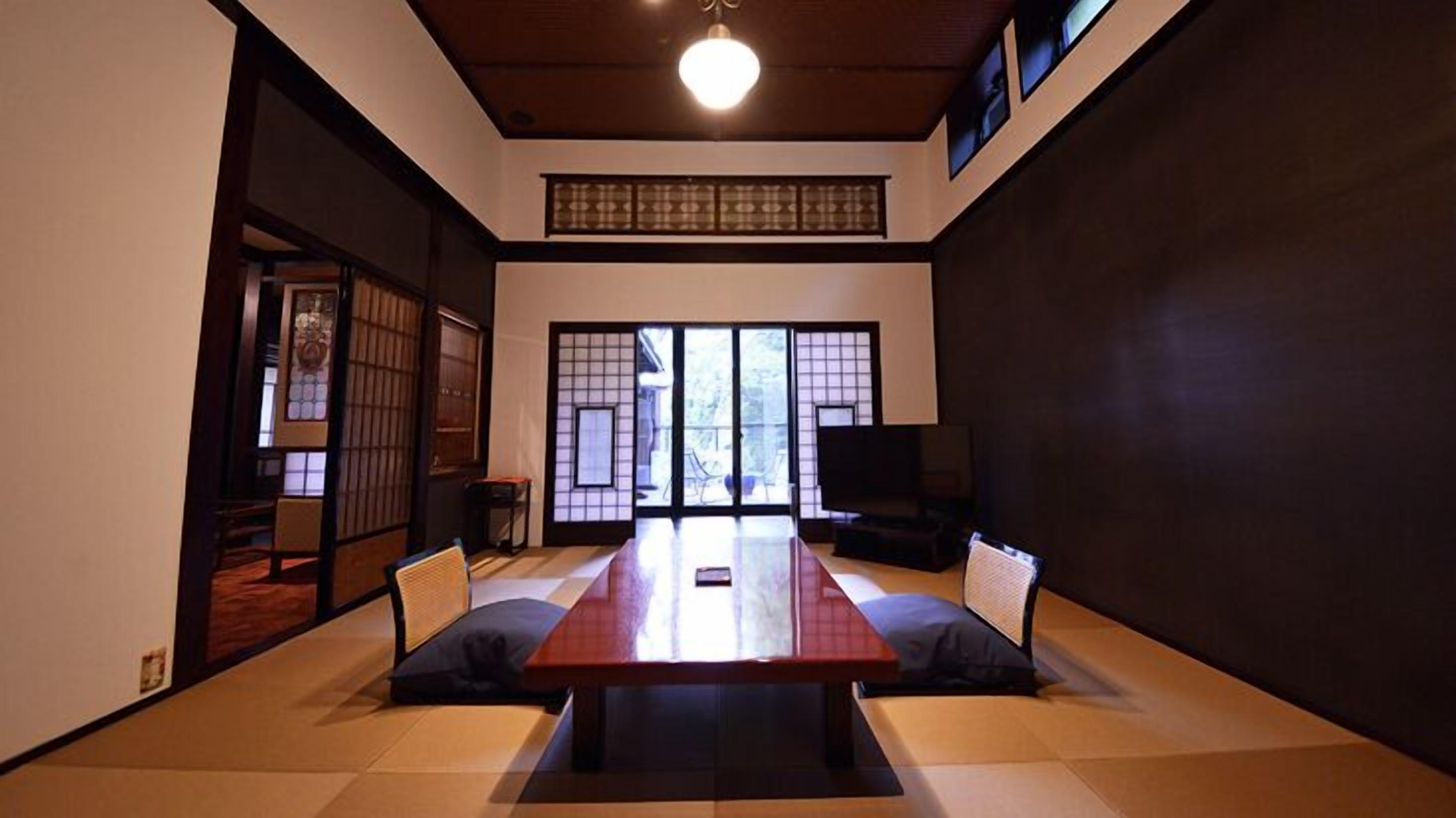 A traditional Japanese-style room with tatami flooring, a low table, sliding doors, and a television.