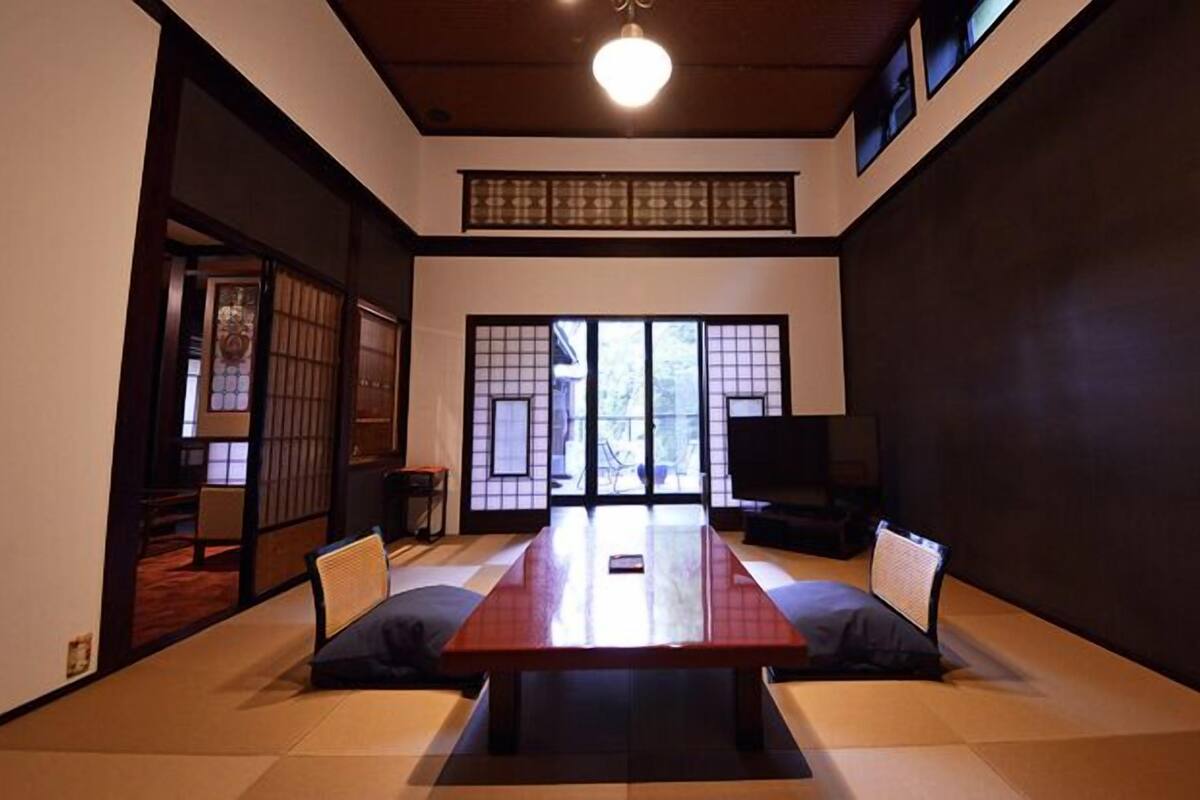 A traditional Japanese-style room with tatami flooring, a low table, sliding doors, and a television.